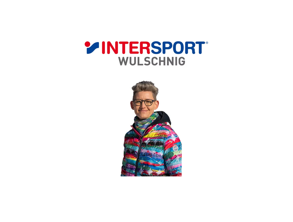 A person smiles while wearing glasses and a colorful, patterned jacket. Above is the blue and red logo of "INTERSPORT WULSCHNIG" on a white background.
