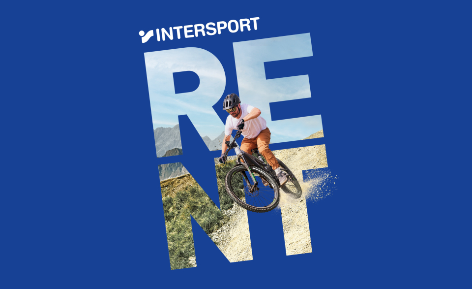 Ein Mountainbiker fährt einen Feldweg hinunter, umgeben von großen, fettgedruckten Buchstaben, die auf blauem Hintergrund das Wort „RENT“ bilden. Eine actionreiche und dynamische Szene.