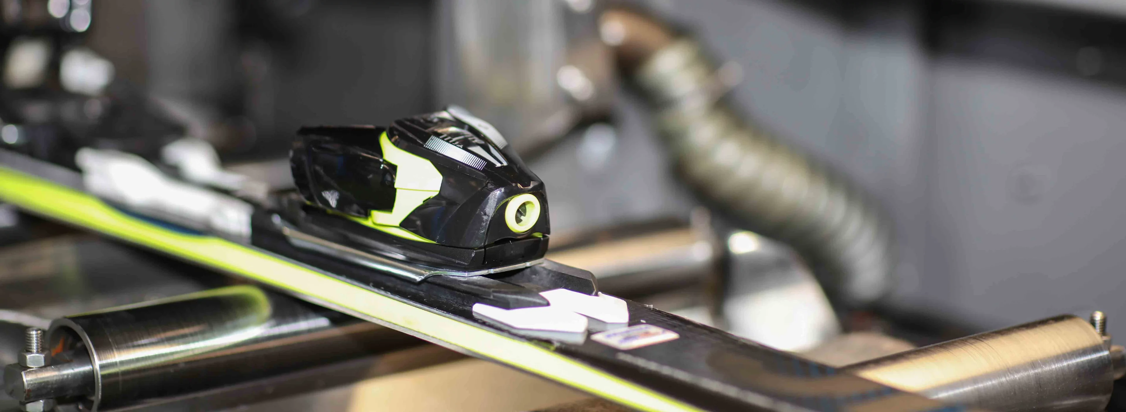 Close-up of a ski binding being serviced in a workshop, focusing on the sleek, modern design and precision machinery. The tone is technical and professional.