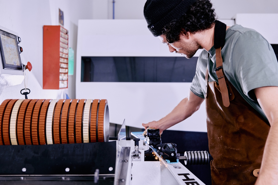 Service employee sharpens a ski on a machine with rotating grinding wheels.